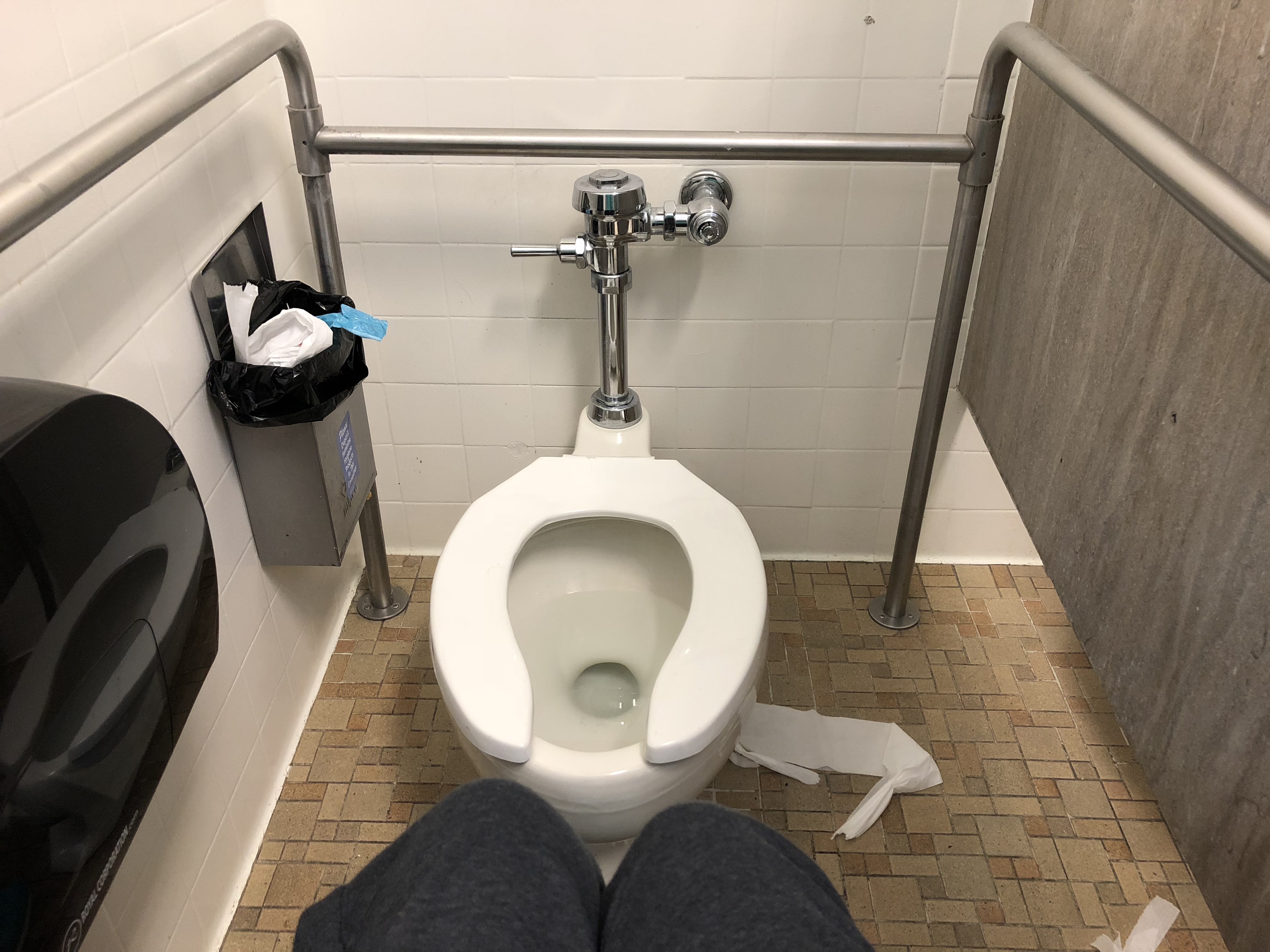 A person in a wheelchair showing how this mobility assisted stall is not large enough to properly accommodate a wheelchair.
