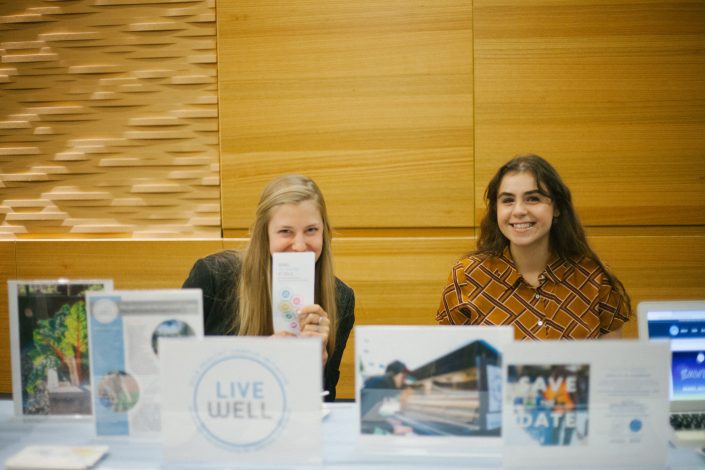 Two women smile in front of table.