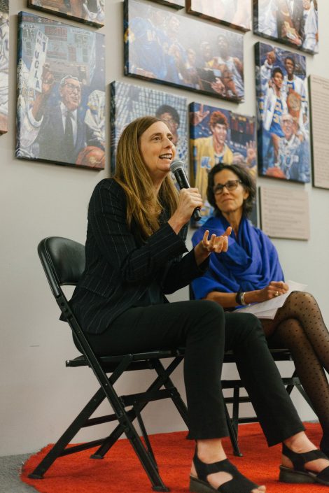 A woman talks through a microphone as another woman sits besides her.