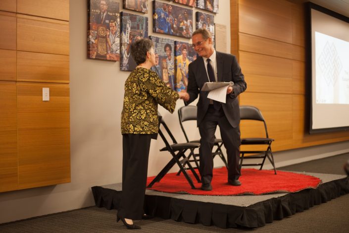 Woman shakes man's hand who holds an award.