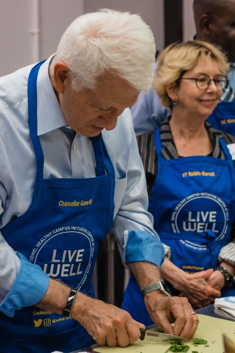 Man cuts on a cooking board with a woman in the background.