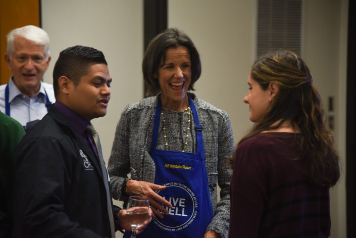 Woman in apron laughs in a circle with a man and woman.