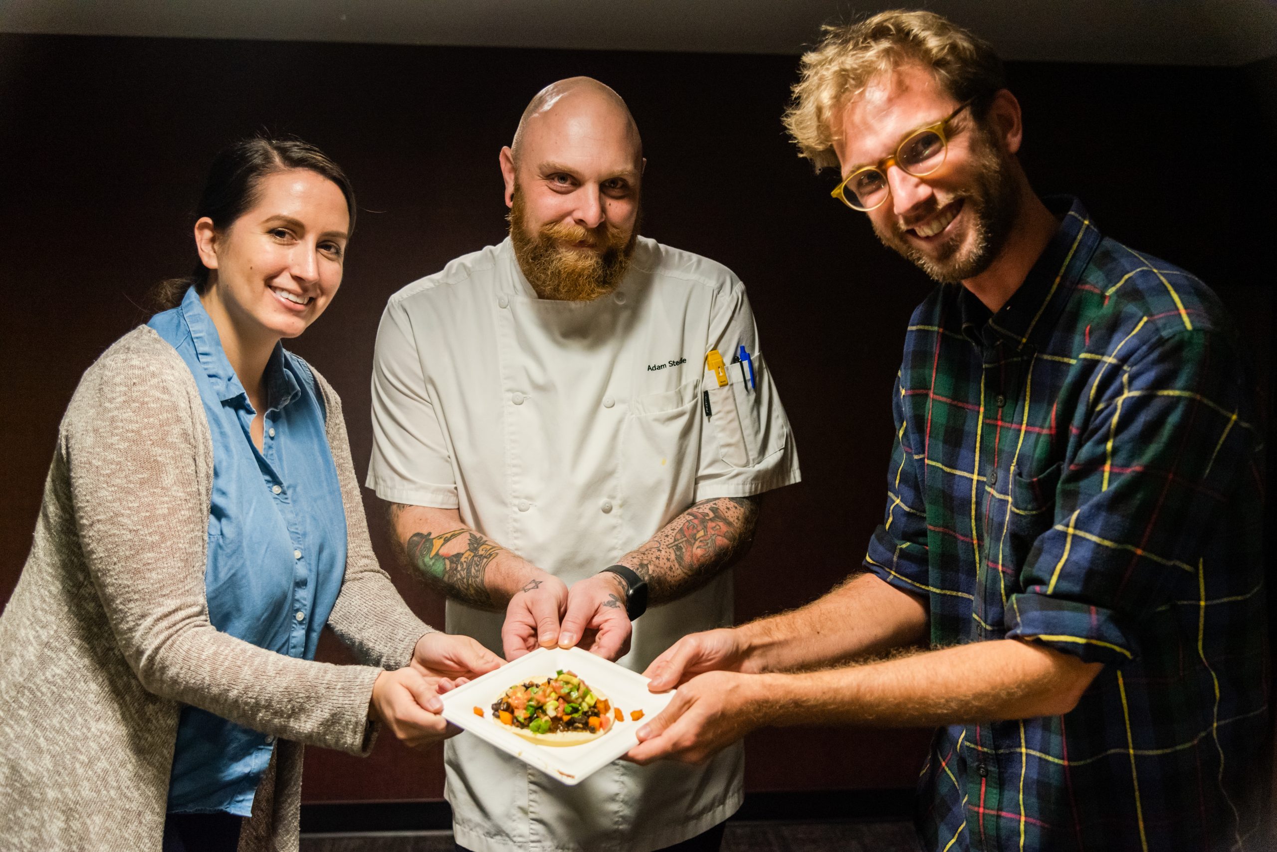 Two women and a man pose with a dish.