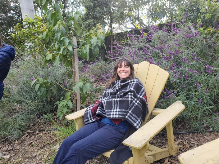 Woman smiles for camera while sitting on garden chair.